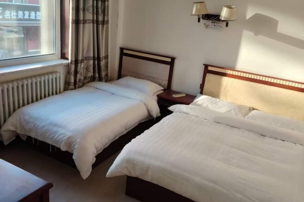 Una habitación de hotel con dos camas, una ventana con cortinas, una lámpara de pared y un radiador.