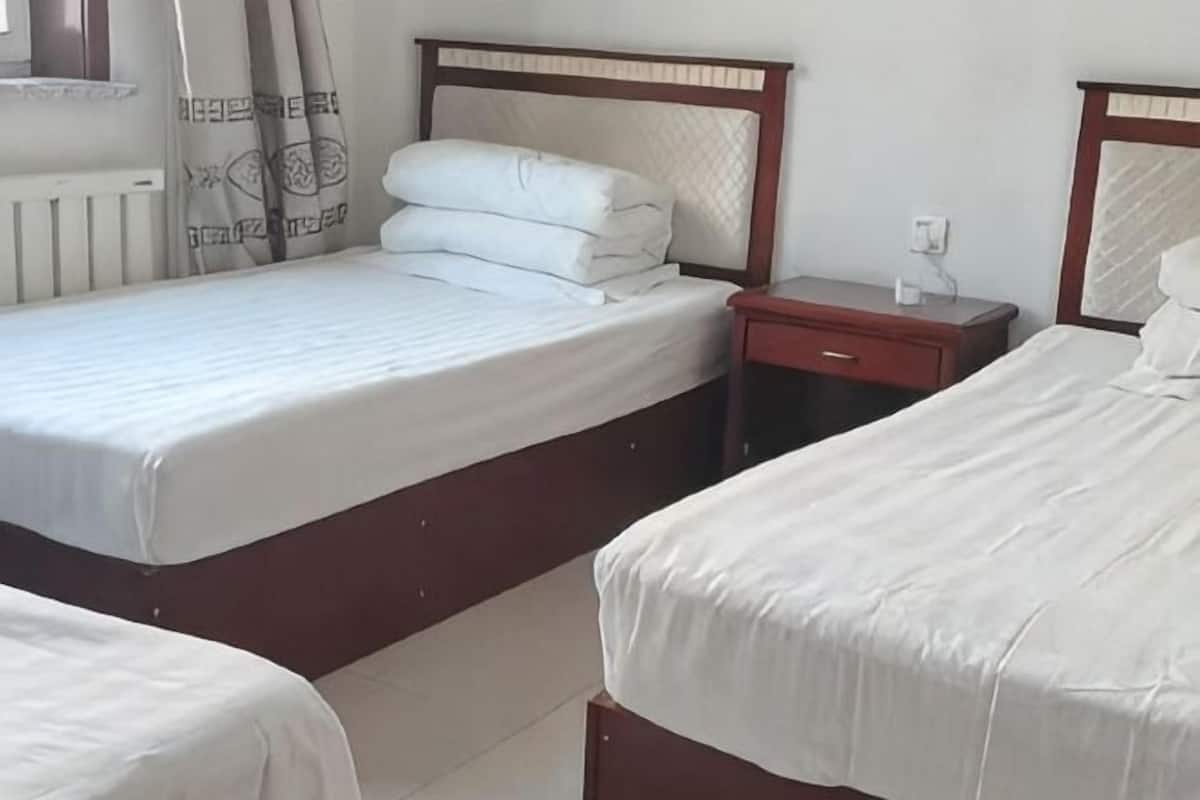 Habitación de hotel con dos camas, una mesita de noche y un ventanal con cortinas.