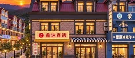 Een hotel met een klassieke architectuur, met een opvallende entree met een rood bord, meerdere ramen en een goed verlichte gevel.