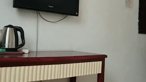 Un televisor montado en la pared, una mesa de madera con un hervidor, y un objeto blanco pequeño sobre la mesa.