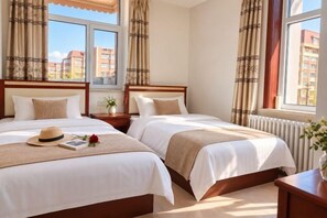 A hotel room with two beds, a window with curtains, a bedside table with a plant, and a hat on one bed. - Aershan Xinda Hotel (Arxan)