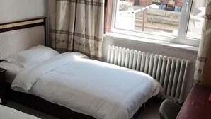Una cama individual con cabecera, una mesita de noche, una ventana con cortinas y un radiador.