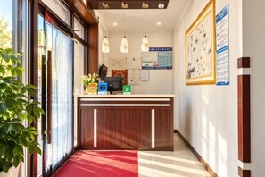 A hotel reception area with a reception desk, a red carpet, and a wall with framed notices. - Aershan Xinda Hotel (Arxan)