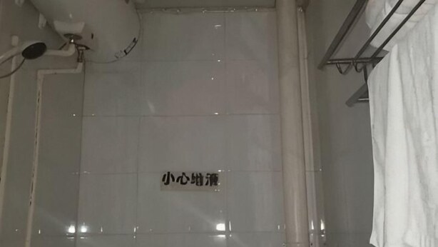 Zona de ducha con azulejos, una señal, un perchero y un cabezal de ducha.