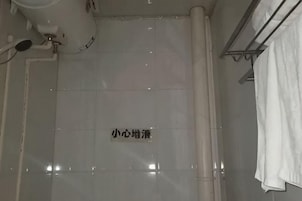 Zona de ducha con azulejos, una señal, un perchero y un cabezal de ducha.