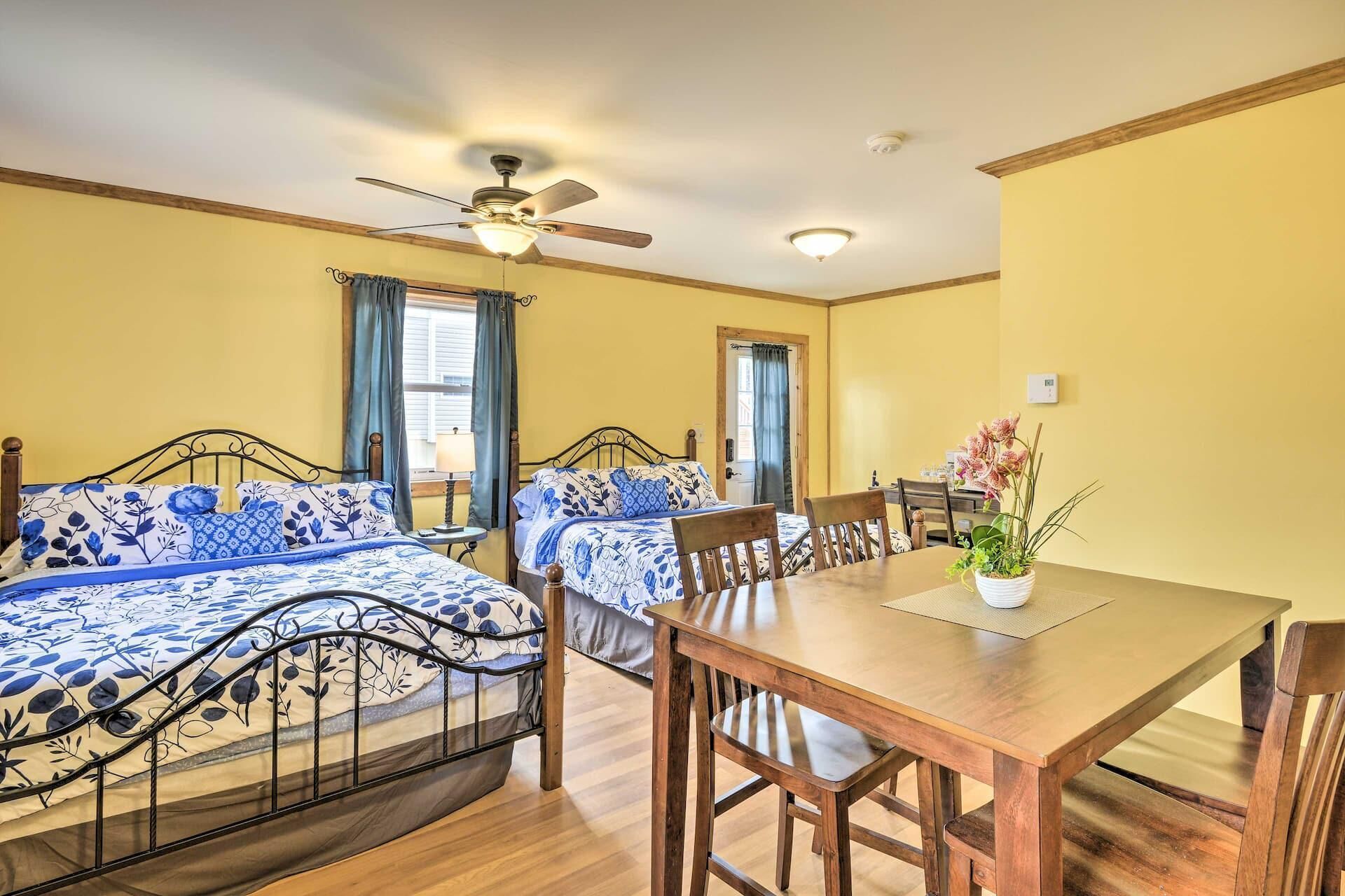 A room with two beds, a dining table, chairs, a ceiling fan, and a potted plant.