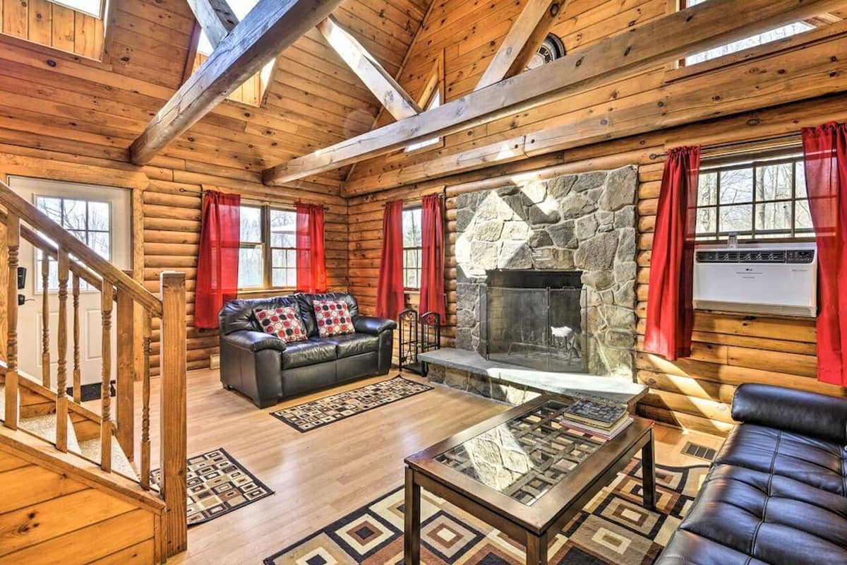 A log cabin interior with a stone fireplace, leather furniture, and a wooden staircase.