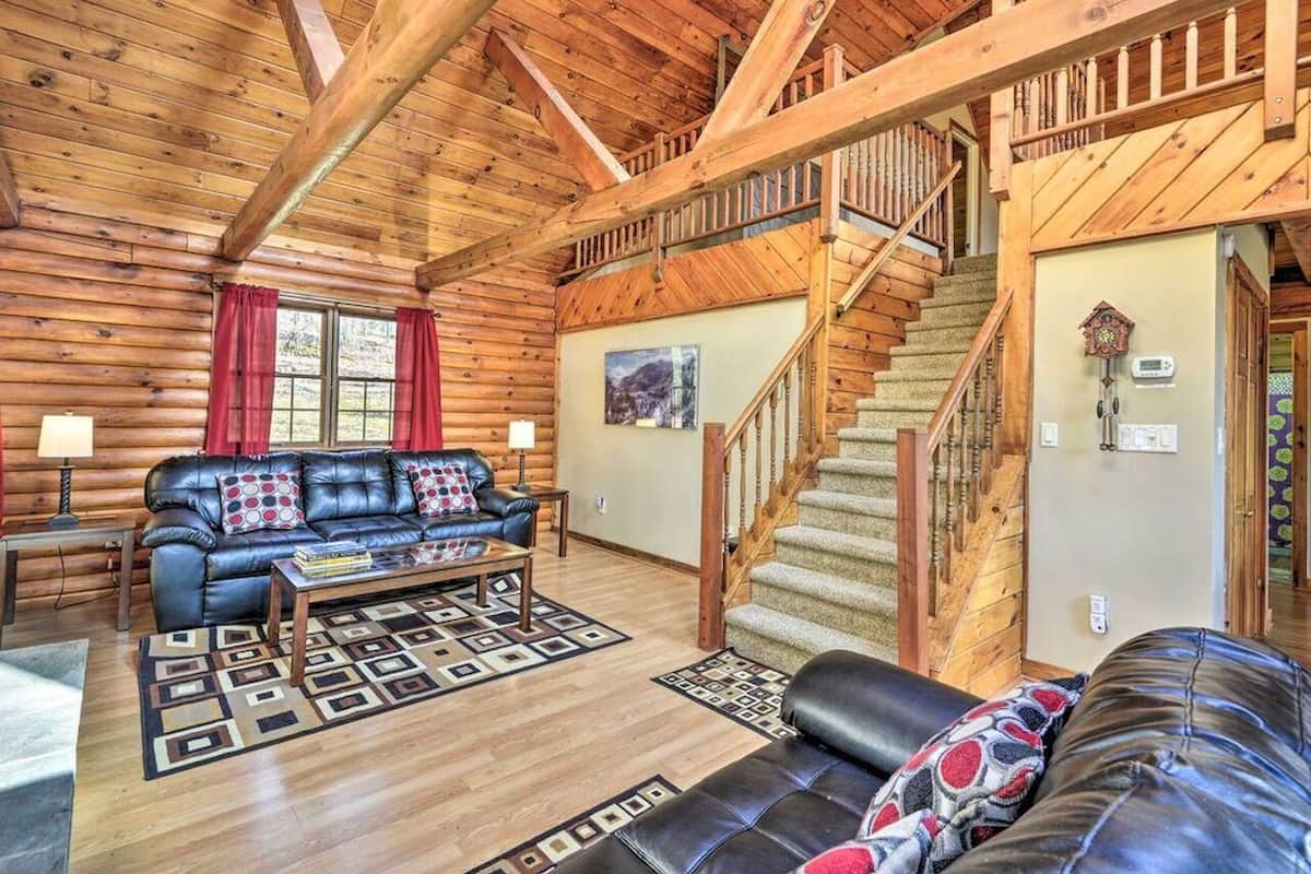 A log cabin interior with a leather sofa, a coffee table, a staircase, and a wooden ceiling.