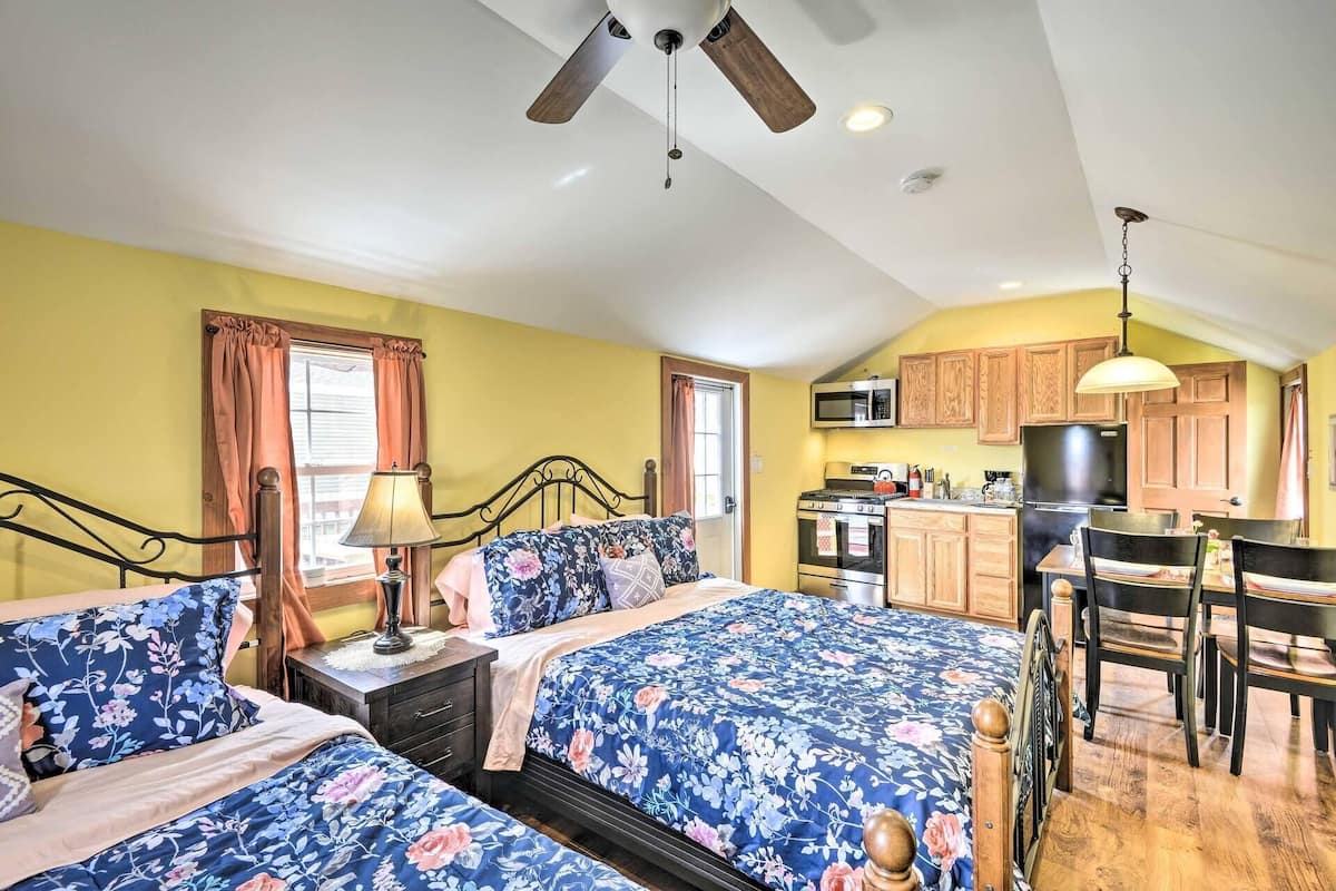 A bedroom with two beds, a desk, and a kitchenette.