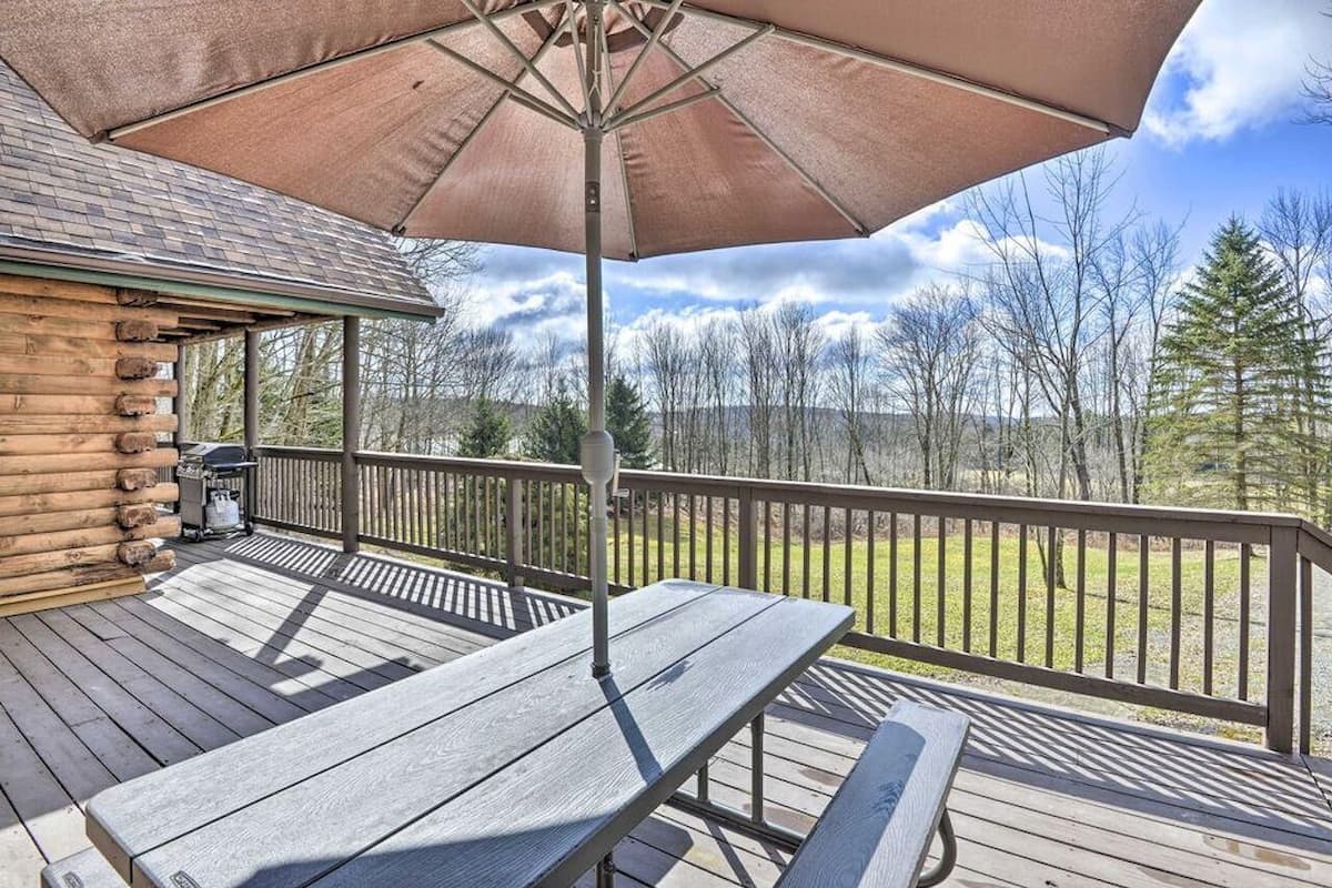 A wooden deck with picnic tables and a large umbrella, overlooking a forested area.