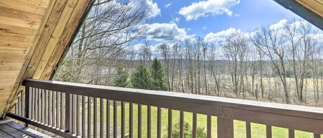 A wooden deck with a railing overlooking a landscape with trees and hills.