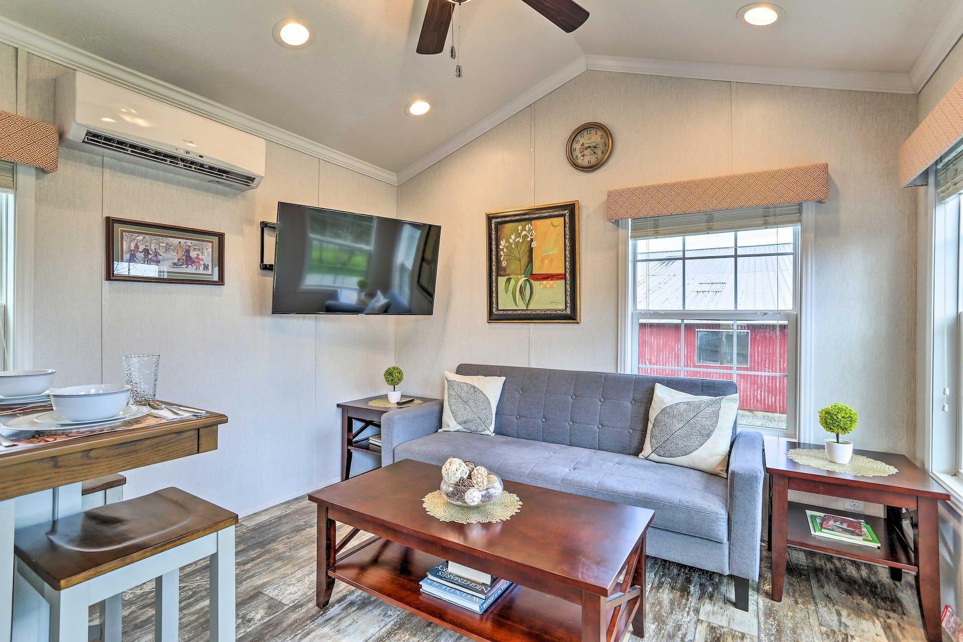A living room with a grey sofa, a wooden coffee table, a TV mounted on the wall, and a window with a view of a red building.