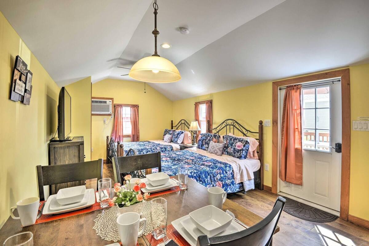 A bedroom with two beds, a dining table set for two, and a television on a stand.