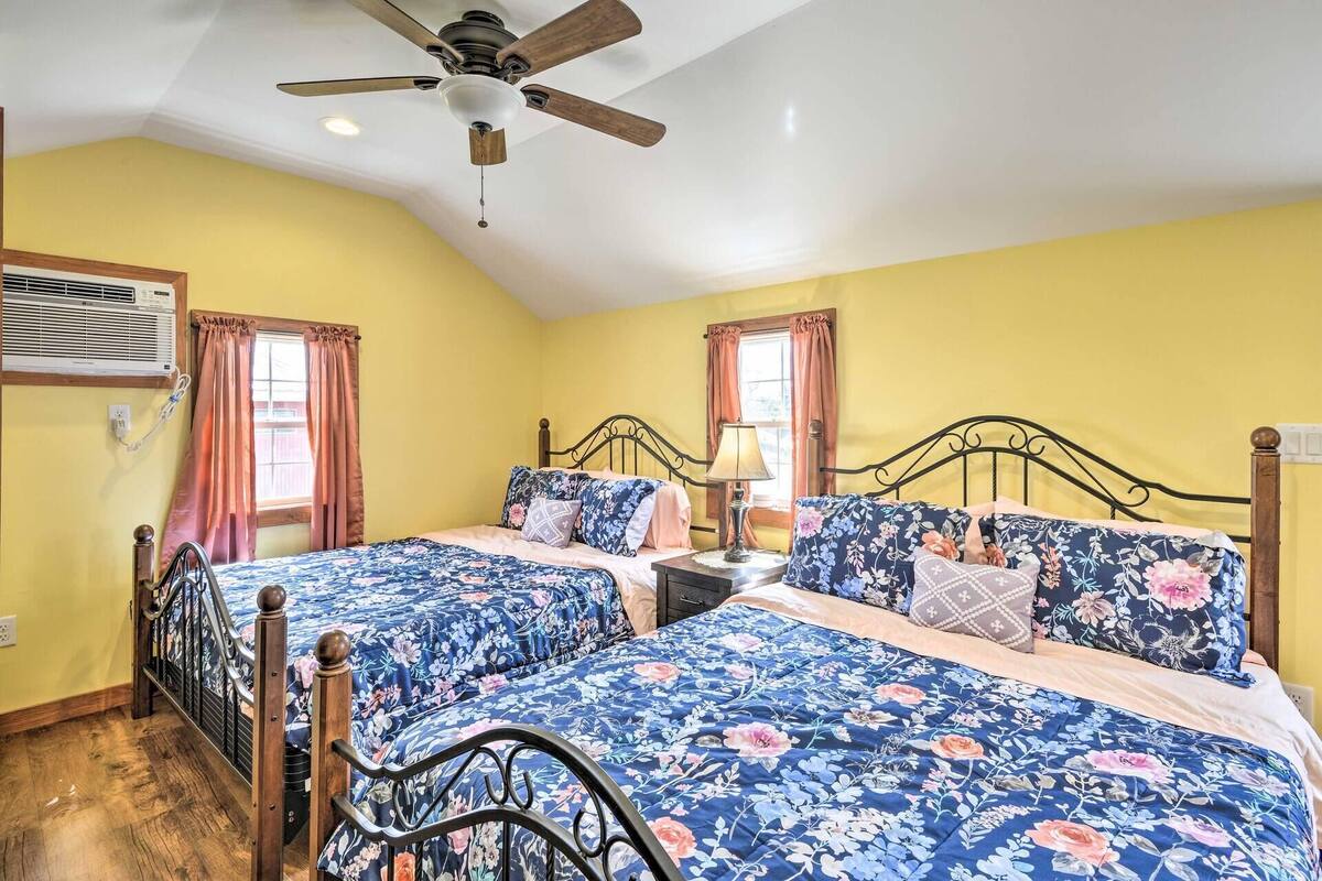 A bedroom with two beds, each with floral bedding, a ceiling fan, and a window with curtains.