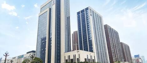 Un edificio moderno de gran altura con fachada de vidrio, situado cerca de una calle concurrida y tráfico de vehículos.