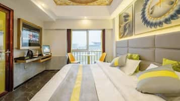 Habitación de hotel con cama, televisión, escritorio y balcón con vistas.