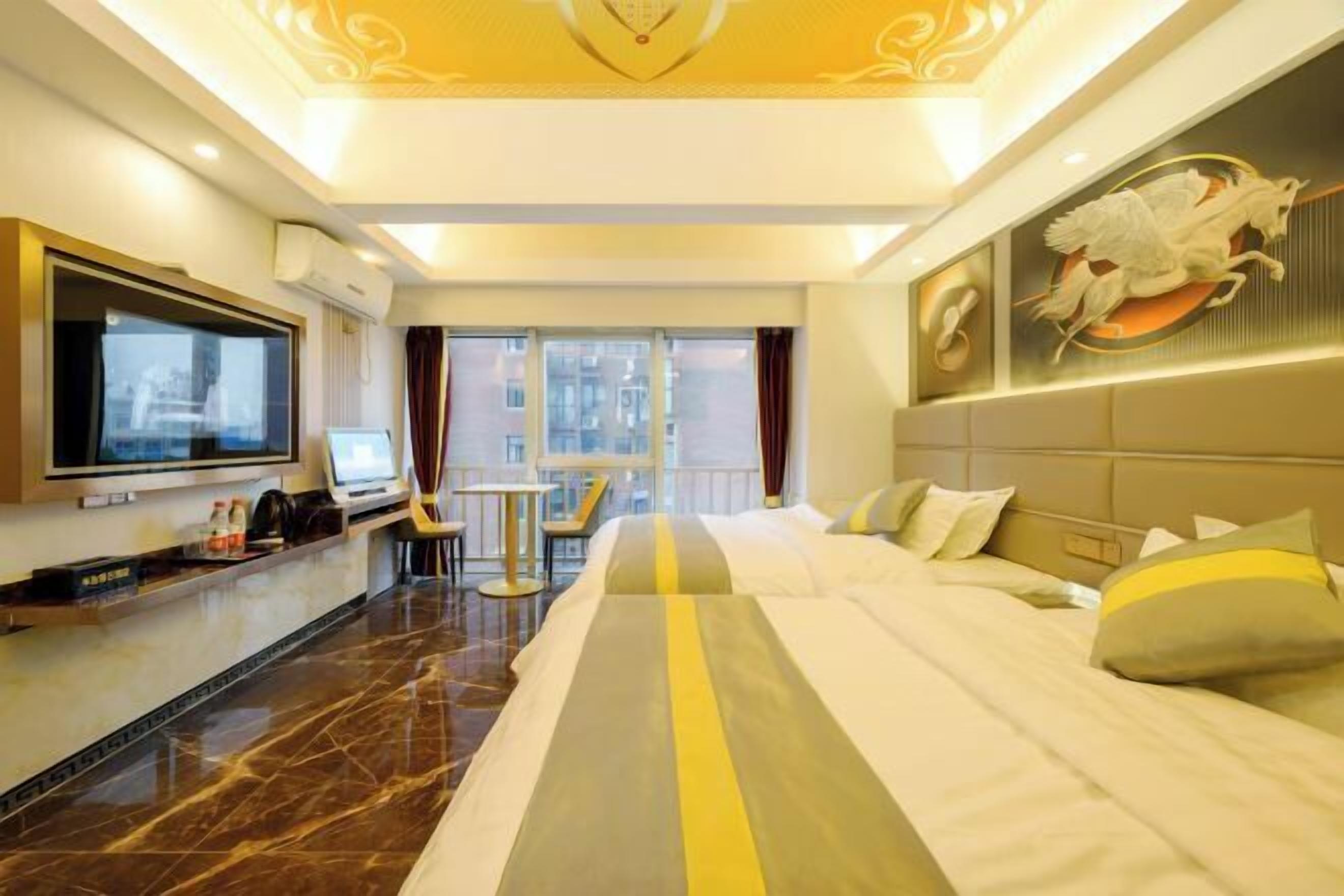 A hotel room with a large bed, a desk with a computer, a TV, and a view of the city through large windows.