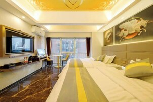 Habitación de hotel con una cama grande, un escritorio con computadora, televisión y vistas a la ciudad a través de amplias ventanas.