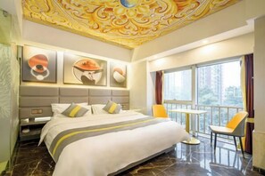 A hotel room with a bed, a small table, chairs, and a balcony with a view. - Bandao Holiday Hotel (Changde)