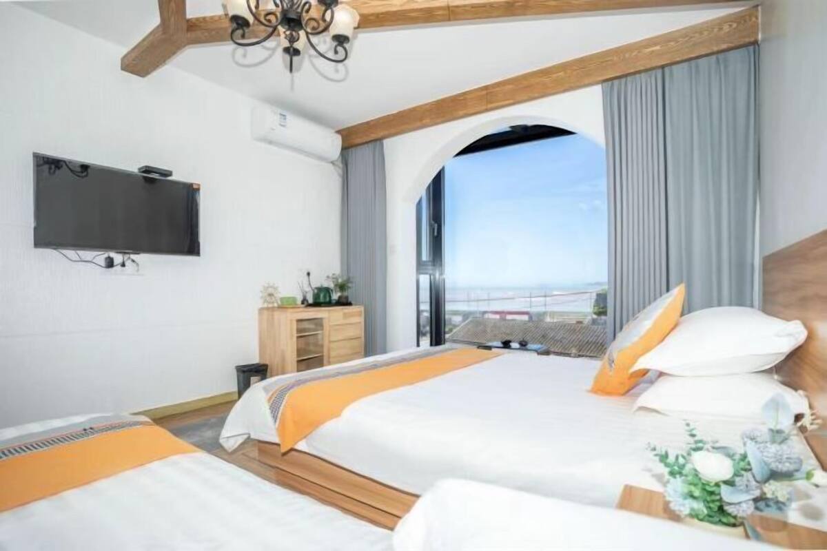 Une chambre d’hôtel avec un grand lit, un téléviseur fixé au mur, un plafond en bois et une vue sur l’extérieur, visible à travers une porte en arc de cercle.