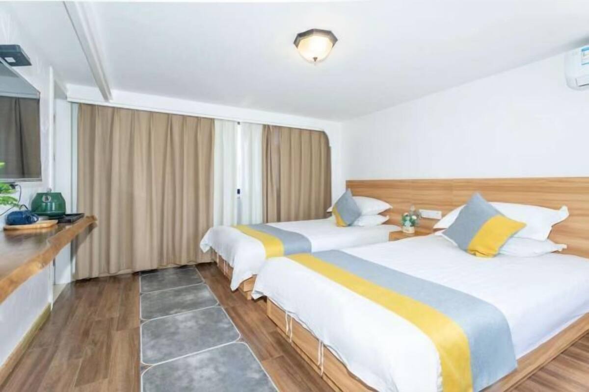 Une chambre d’hôtel avec deux lits, une tête de lit en bois, une petite table avec une bouilloire et une fenêtre avec des rideaux.