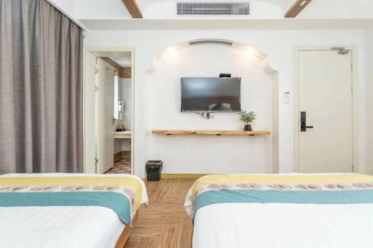 Une chambre d’hôtel avec deux lits, un téléviseur fixé au mur, une petite étagère et une porte sur le côté droit.