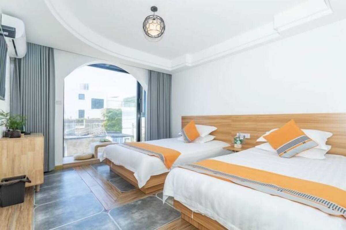 Une chambre d’hôtel avec deux lits, une tête de lit en bois, une petite table de chevet et une vue sur l’extérieur grâce à une grande fenêtre.
