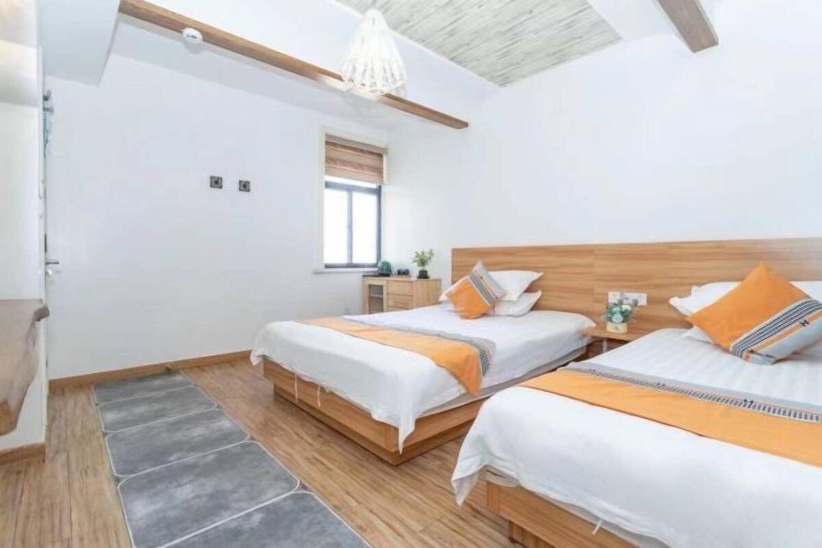 Une chambre moderne avec deux lits, un plancher en bois, une fenêtre avec des stores et un luminaire suspendu.
