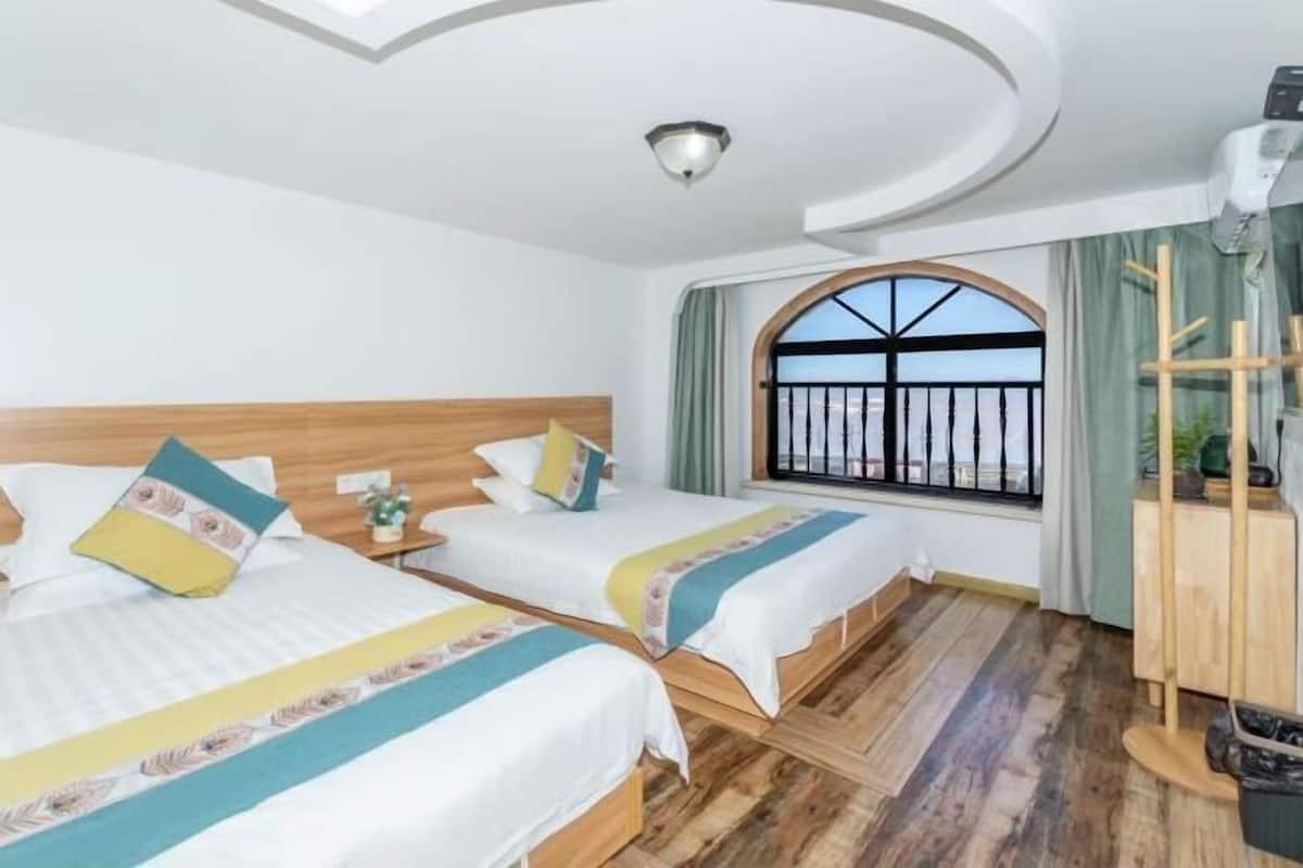 Une chambre d’hôtel avec deux lits, une tête de lit en bois, une grande fenêtre donnant sur un beau paysage et un luminaire au plafond.