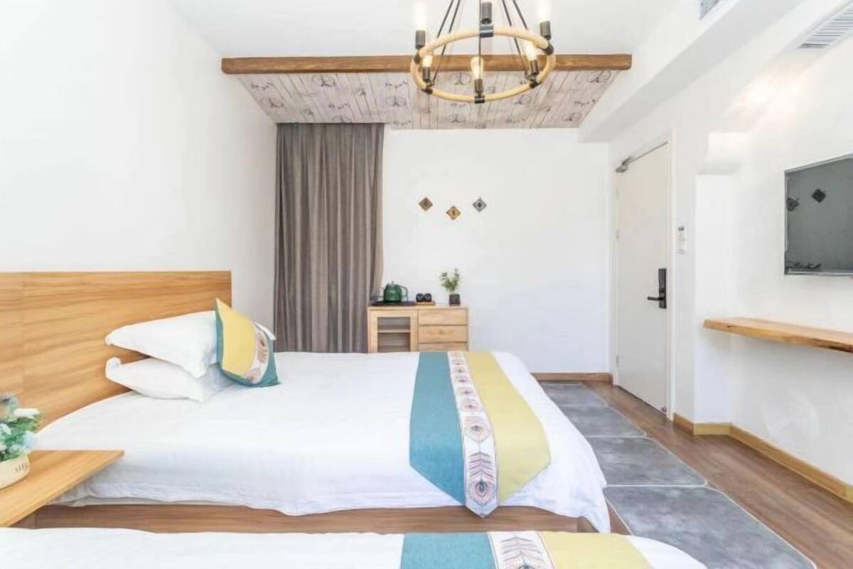 Une chambre avec une tête de lit en bois, un lit avec une literie à motifs, une table de chevet, une petite table avec une plante, un téléviseur fixé au mur et un luminaire suspendu au plafond.