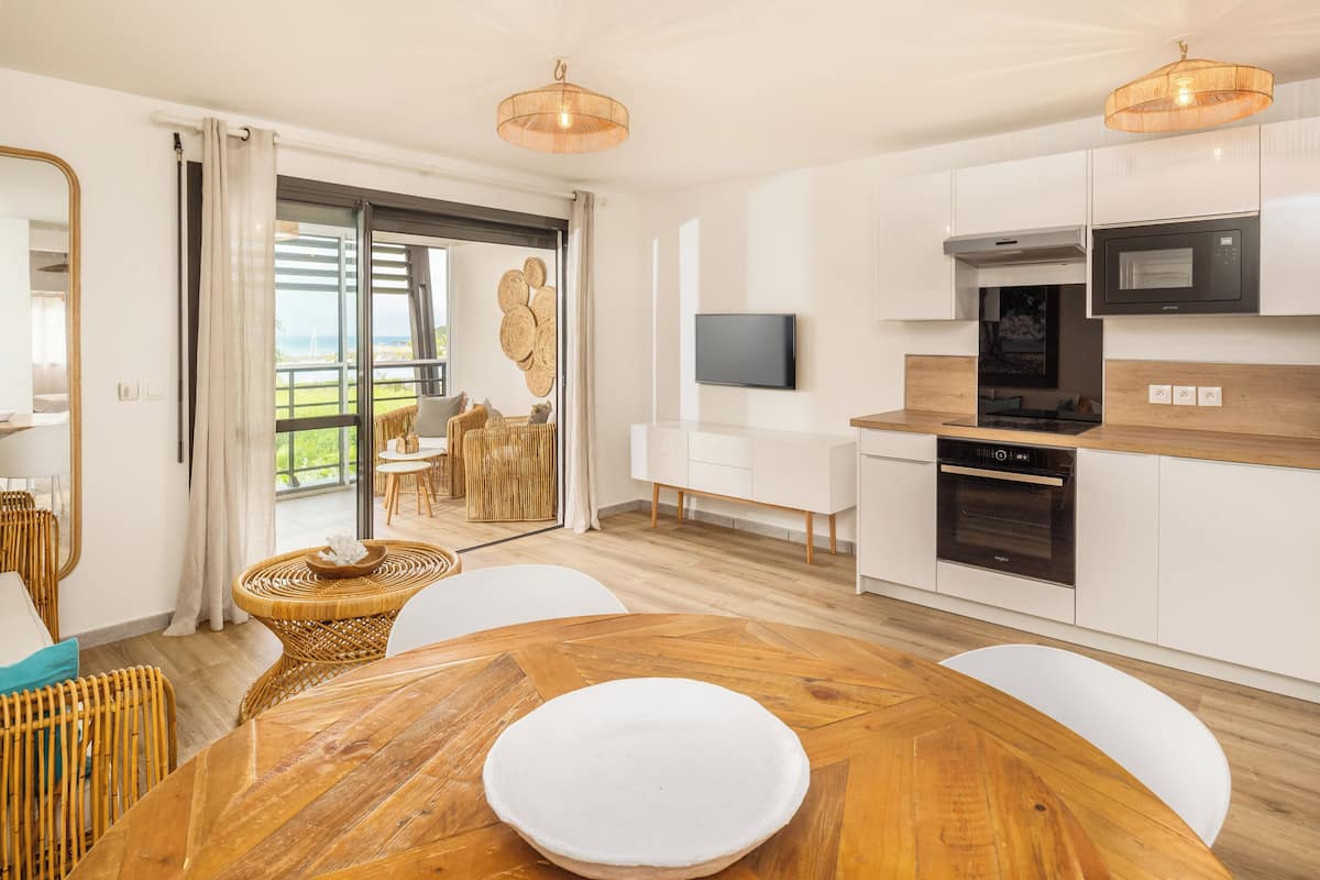 Een moderne keuken met witte kasten, een inbouwoven en een magnetron. Er is een zithoek met een houten tafel en witte stoelen.