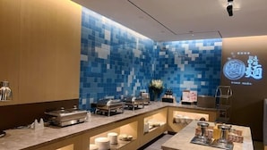 Un moderno vestíbulo de hotel con una pared de azulejos azules, mostradores de buffet y una pantalla de proyección mostrando texto.