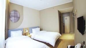 Habitación de hotel con dos camas, un adorno circular en la pared, un televisor de pantalla plana y una mesita con una taza y un hervidor.