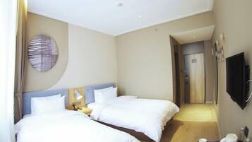 A hotel room with two beds, a round wall decoration, a flat-screen TV, and a small table with a cup and a kettle.