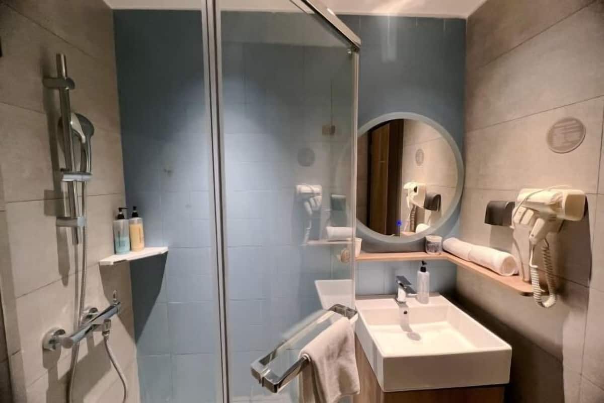 Uma casa de banho moderna com cabine de chuveiro em vidro, um espelho redondo, uma pia e um porta-toalhas.