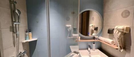 A modern bathroom with a glass shower enclosure, a round mirror, a sink, and a towel rack.