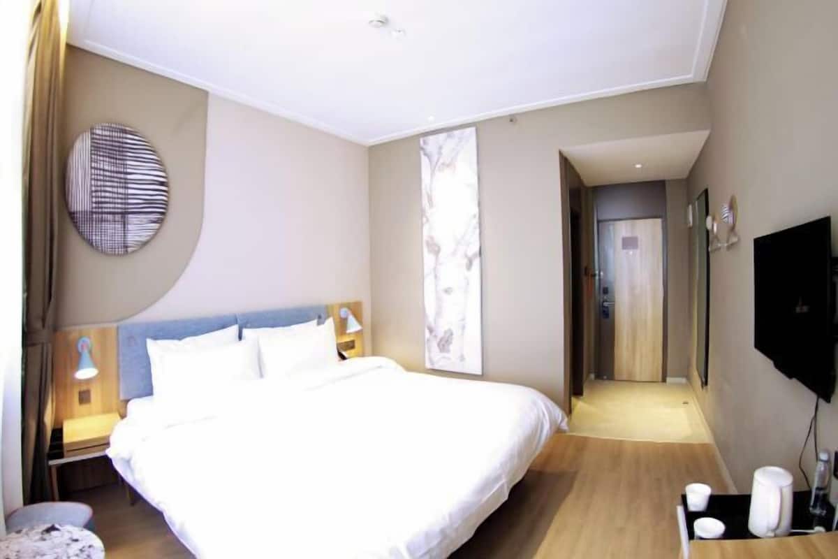 Quarto de hotel com cama, luminárias de cabeceira, TV de tela plana, obra de arte na parede e janela com vista.