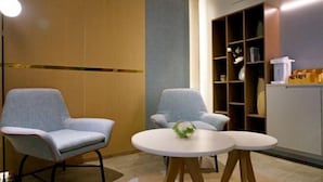 Una habitación moderna con dos sillones grises, una mesa redonda con un florero y un aparador con estantes.