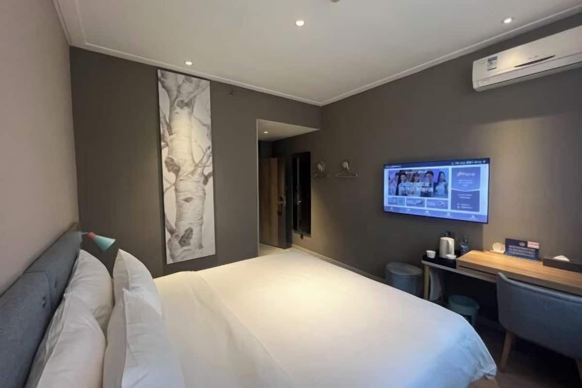 Quarto de hotel moderno com uma cama grande, uma escrivaninha e uma televisão exibindo um cardápio.