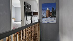 Une pièce avec un lit, une porte et un tableau représentant un paysage enneigé avec une tour.