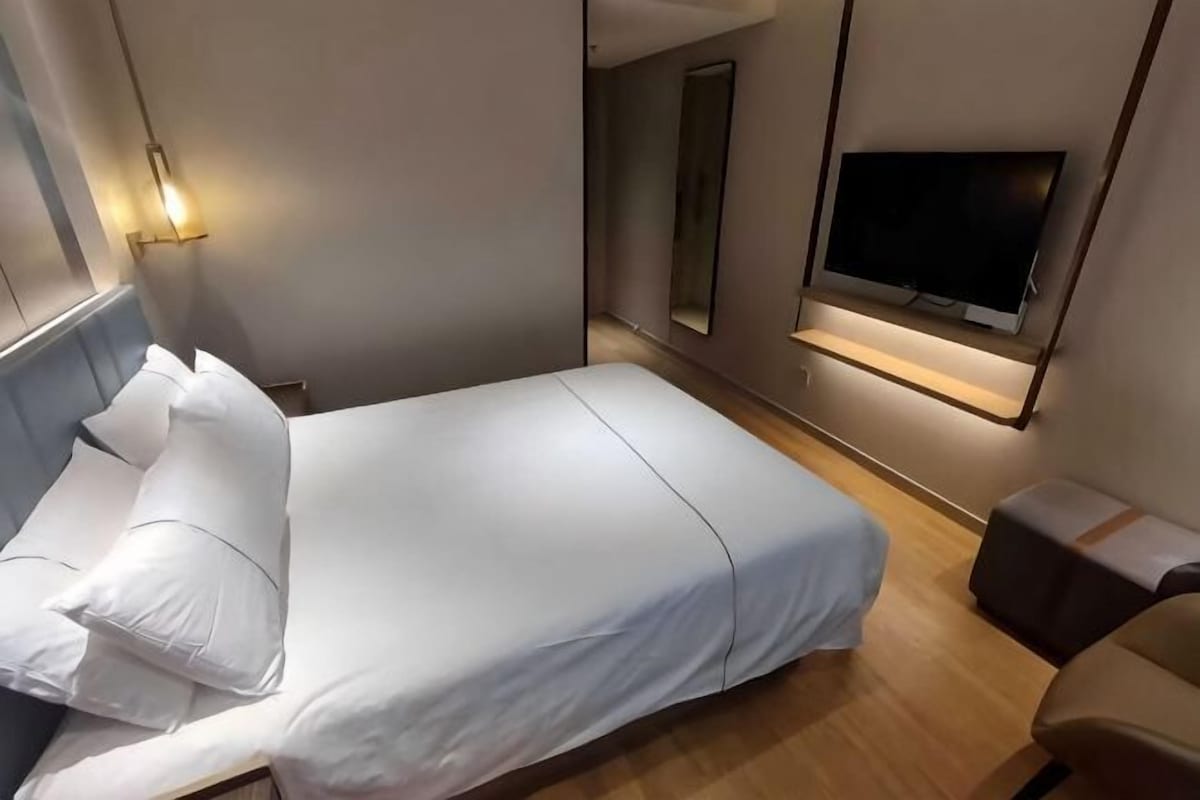 Une chambre d’hôtel avec un lit, un téléviseur fixé au mur et une table de chevet.