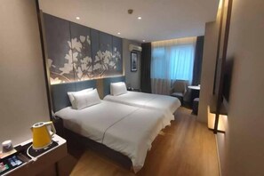 Habitación de hotel con dos camas, un escritorio con cafetera, televisor y un diseño floral en la pared.