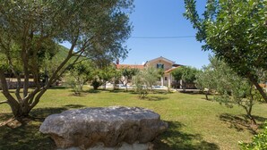 A stone bench in a grassy area with trees and a building in the background. - Villa Bosnjak with a private pool (Osoje)