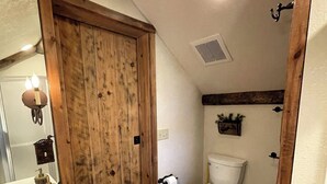 A bathroom with a wooden door, a toilet, a sink, and a mirror.