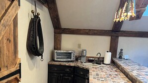A compact kitchen with a rustic wooden ceiling, a built-in stove, a toaster, and a hanging bag.