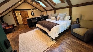 A bedroom with a loft-style ceiling, wooden beams, a bed with multiple pillows, a desk, and a chair.