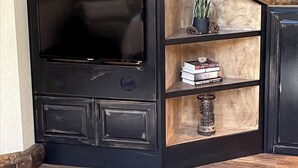 A black entertainment unit with a flat-screen TV, shelves with decorative items, and a wooden floor.