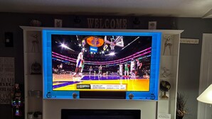 A living room with a large flat-screen TV mounted on a white wall, displaying a basketball game. - 4m Disney : Private Pool, Hot Tub, Game Room & Fast WiFi, pets, Guests favorite (Kissimmee)