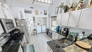 A modern kitchen with white cabinets, a black countertop, and stainless steel appliances. There is a small island with a sink and a decorative mat. - 4m Disney : Private Pool, Hot Tub, Game Room & Fast WiFi, pets, Guests favorite (Kissimmee)