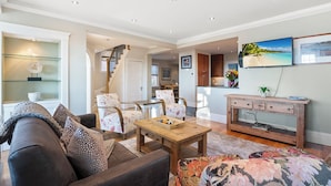 A spacious living room with a sofa, chairs, a coffee table, and a staircase leading to an upper level. - Magnificent Ocean View; Walk to beaches and town (Swampscott)